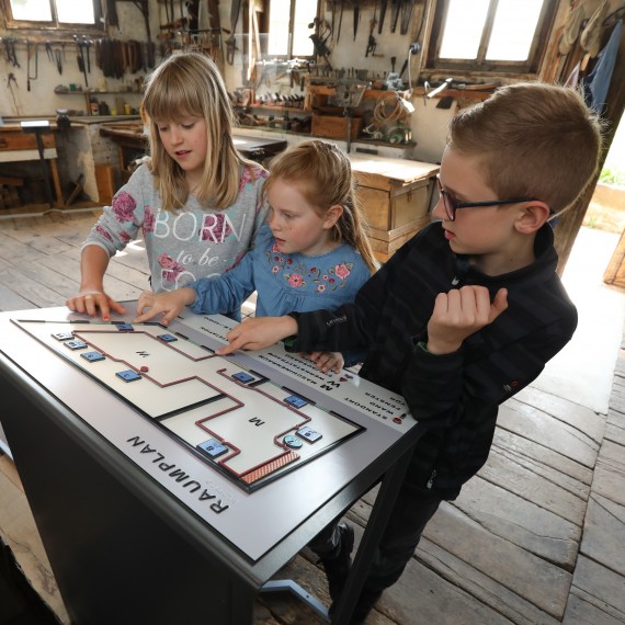 Drei Kinder berühren einen tastbaren Lageplan in einer historischer Werkstatt.