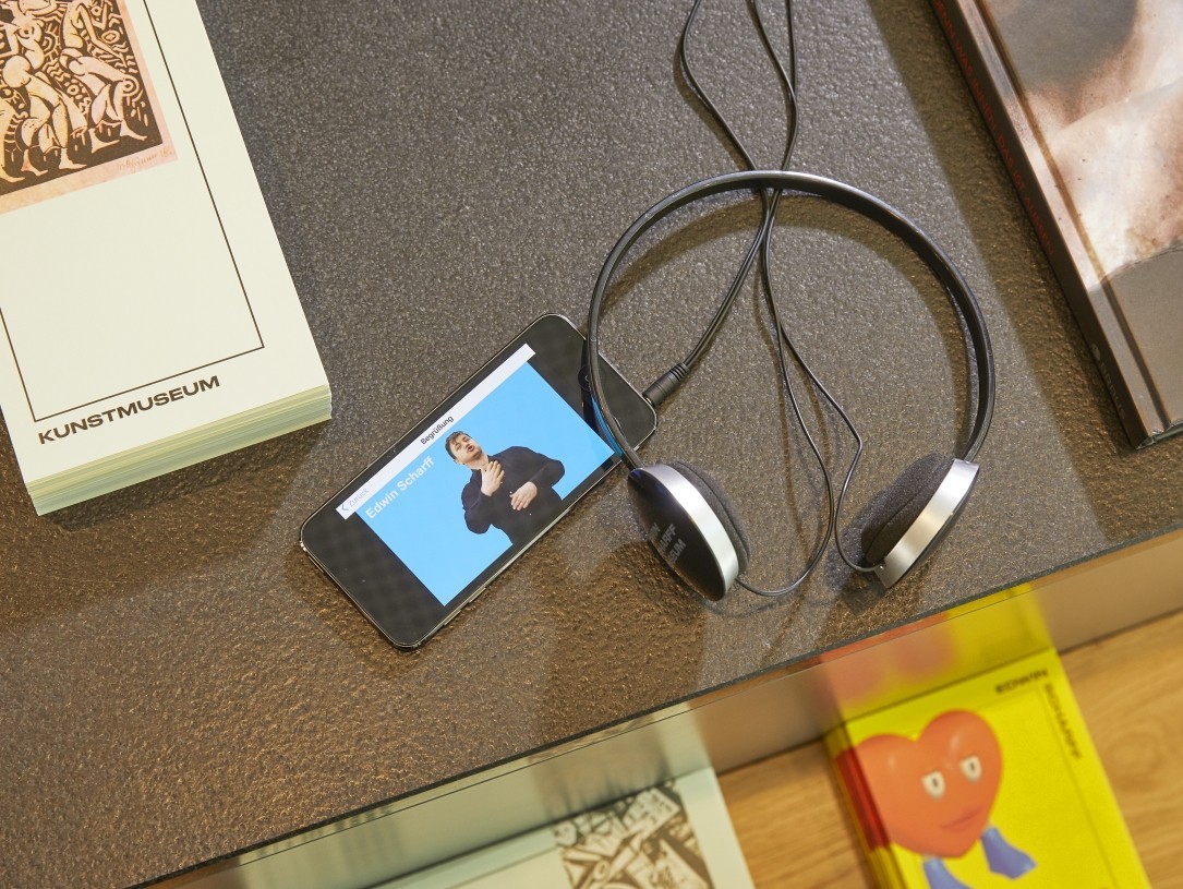 Ein Kopfhörer und ein Smartphone, auf dem ein Video mit Deutscher Gebärdensprache zu sehen ist.