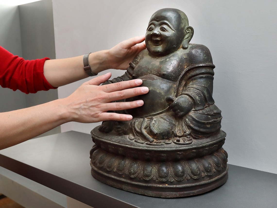 Zwei Hände berühren eine Buddha-Figur.