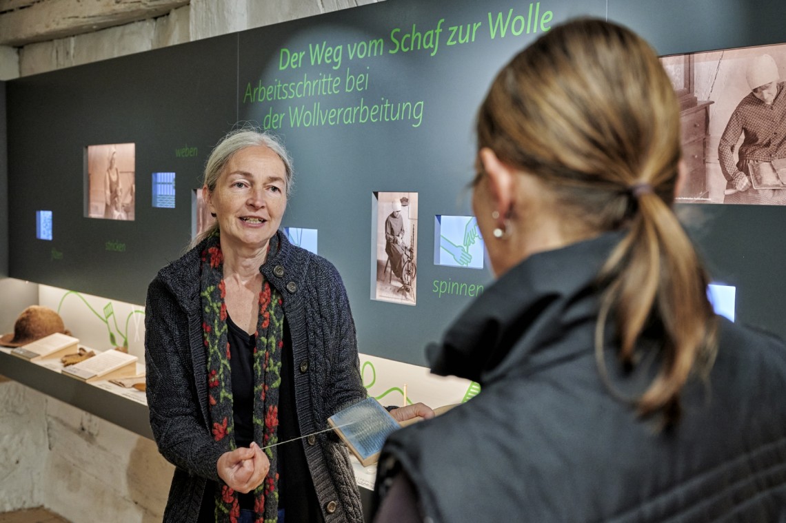 Eine Frau erklärt einer Museumsbesucherin den Wollkamm.