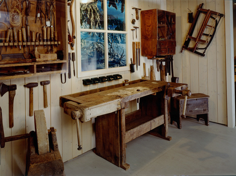 Eine Werkbank umgeben von Regalen und Werkzeugen.